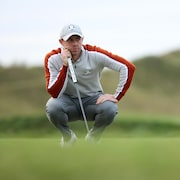 Rory McIlroy accroupit, bâton de golf à la main à la Coupe Ryder.