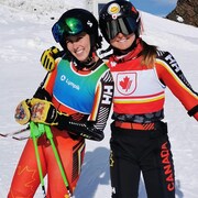 Deux skieuses souriantes, en combinaison de vitesse, posent pour la photo sur une pente enneigée.