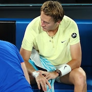 Un joueur de tennis, assis et résigné, est soigné au poignet sur le terrain.