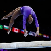 Une gymnaste fait un périlleux arrière au-dessus de la poutre.