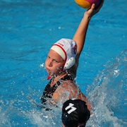Une joueuse de water-polo tient le ballon dans sa main droite.
