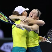 Les deux joueuses de tennis, en jaune et vert, s'enlacent après avoir gagné leur match. 