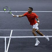 Félix Auger-Aliassime frappe la balle et son coéquipier Ben Shelton est en position à l'arrière-plan.