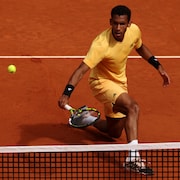 Un joueur de tennis effectue un amorti près du filet et suit la balle des yeux.