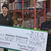 Deux hommes tiennent un énorme chèque après le don d'un joueur de hockey pour un organisme.