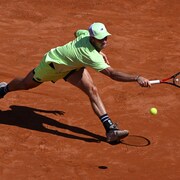 Un joueur de tennis allonge le bras pour frapper la balle du revers.
