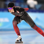 Une patineuse de vitesse, vêtue d'une combinaison noir et rouge, participe à une course 