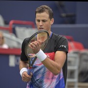 Un joueur de tennis tient sa raquette d'une main et pose l'autre sur les cordages.