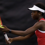 Une joueuse de tennis vêtue de rouge et de blanc s'apprête à faire un service avec sa raquette rouge et jaune. 