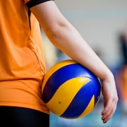 Un enfant tient un ballon de volleyball avec son bras droit.