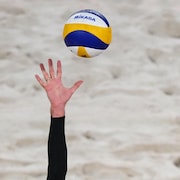 Un joueur de volleyball de plage étire un bras pour tenter de toucher au ballon pendant un match.