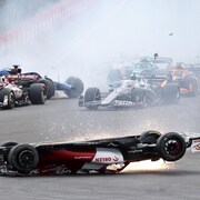 L'Alfa Romeo rouge et blanche de Zhou, à l'envers, glisse en faisant une pluie d'étincelles, alors que derrière, un nuage de fumée cache le peloton de voitures au premier virage du Grand Prix. 