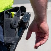 Gros plan sur l'arme à la ceinture d'un policier et sa main à proximité.