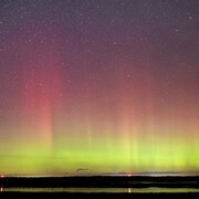 Une aurore boréale. Il y a un dégradé de jaune, de rose et de violet. L'image est aussi constellée d'étoiles.