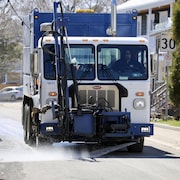 Un col bleu nettoie une rue à bord d'un camion.