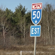Des arbres en bordure de l'autoroute 50, un panneau indique l'autoroute 50 en direction Est.