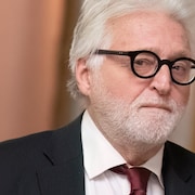 Gilbert Rozon regarde de côté dans un couloir du palais de justice de Montréal, l'air sérieux.