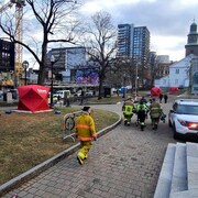 Des tentes de sans abri rouge, et des pompiers emmènent sur un brancard une victime. 