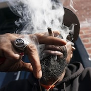 James Malone, dont on voit la main en avant-plan tenant un joint, fume.