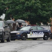 Des policiers sont proches d'une voiture de police, avec un appareil photo en main.