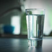 Un verre d'eau sur un comptoir, près d'un robinet.