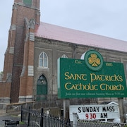 Une église en briques rouge de côté et un panneau vert avec le nom de l'église au premier plan.
