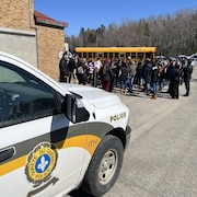 Des élèves rassemblés à l'extérieur, entre un autobus scolaire et un véhicule de la SQ.