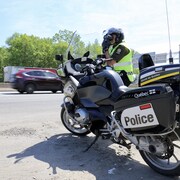 Un policier à moto fait de la surveillance radar pendant que des véhicules circulent derrière lui sur l'autoroute. 