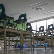 Des chaises montées sur des bureaux dans une classe vide.