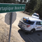 Deux véhicules de police bloquent l'accès de la route Portapique Beach près d'un panneau indicateur.