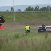 Un policier dans un champ en bordure d'une autoroute, le 18 juin 2025.