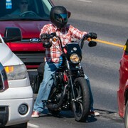 Un motocycliste immobilisé attend de démarrer entre deux voitures. 