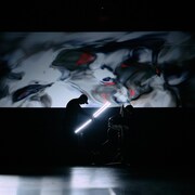 On voit une silhouette dans l'ombre, avec une projection en arrière-plan.