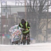 Un homme marche dans une rue en traînant un vélo chargé de canettes.