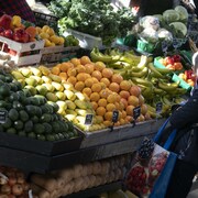 Une femme devant des étals de fruits et légumes.