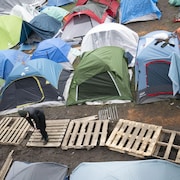 Des tentes regroupées, avec des passerelles en bois à l'avant, sur un terrain en bouette.