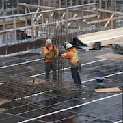 Deux travailleurs manipulent des matériaux sur un chantier. 