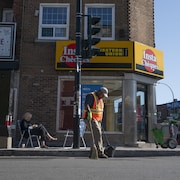 La journaliste Émilie Dubreuil est assise sur une chaise devant un comptoir de transfert d'argent Western Union. Devant elle, un homme balaie le sol.