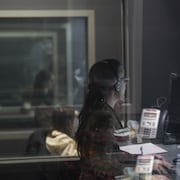 Une femme assise devant un écran, dans la pénombre d'un studio.