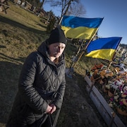 Des fleurs surmontées de drapeaux ukrainiens ornent une tombe.