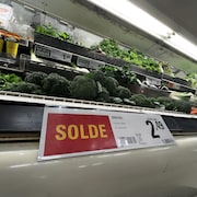 Une étagère de légumes dans une épicerie, devant laquelle on voit une pancarte «Solde».