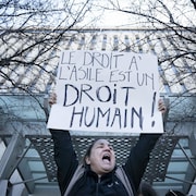 Une manifestante réclamant de respecter les droits des demandeurs d'asile lors d'une manifestation devant les bureaux de circonscription du premier ministre Justin Trudeau.
