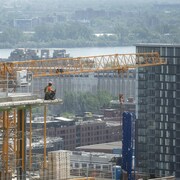 Un ouvrier de la construction travaille sur un immeuble en hauteur et on aperçoit une grue à l'arrière.