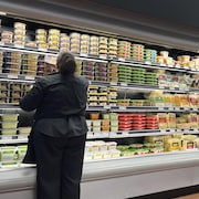 Une femme devant un frigo dans une épicerie.