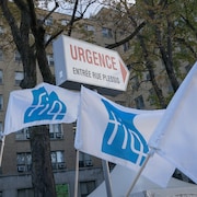Trois banderoles de la FIQ, dans le vent, devant les urgences d'un hôpital.