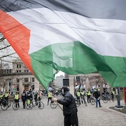 Une rangée de policiers est postée devant la grille du campus de l'Université McGill pendant qu'un manifestant, le visage partiellement recouvert d'un keffiyeh, brandit un drapeau palestinien.