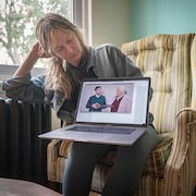 Catherine Dorion, assise dans son salon, tient un ordinateur affichant une photo de Gabriel Nadeau-Dubois avec Manon Massé.