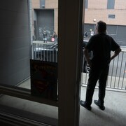 Un homme sur son balcon observe la rue.
