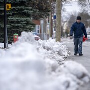 Un jeune homme qui marche dans la rue à côté d'une petite montagne de neige sur un trottoir.