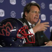 Un homme parle lors d'une conférence de presse, avec à ses côtés un casque des Alouettes.